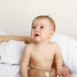 Cute nice little baby girl crying lying with her mom on bed at home.