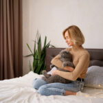 Pets, morning, comfort, rest and people concept - happy young woman with cat in bed at home