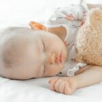 The newborn baby slept on a white bed and hugged the bear.