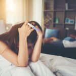 Sad woman complaining holding a pregnancy test sitting on bed