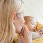 Above view of young mother kissing her baby's hand