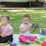 Babys, less than a year old, playing with a toys on a background of green grass