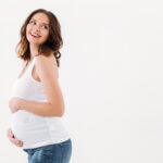 Picture of amazing happy pregnant woman standing isolated over white background. Looking aside.
