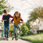 Brother and sister in a park. Boy with scooter. Girl with bicycle.