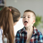 Doctor consults little boy with sore throat. Inflammation of tonsils of adenoids and tonsillitis in children