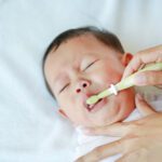 Close-up mother hand clean baby teeth and tongue with soft rubber brush.