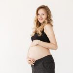 Close up portrait of happy handsome young mother with blonde wavy hair in black sport clothes holding stomach with hands, looking in camera with relaxed expression. Beauty and health.