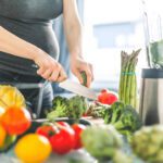 Young pregnant woman cooking healthy meal food vegetables in the kitchen. Lifestyle background. Horizontal