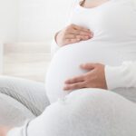 Pregnant woman holds her hands on her swollen belly on white bed, Love and feel joyful as emotional well affect to baby neurological and psychological development