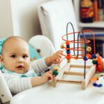 Baby boy playing toys in a high chair at home