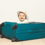 Baby girl sitting in suitcase on the floor with empty background.