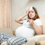 pregnant woman sitting on sofa with thermometer in living room